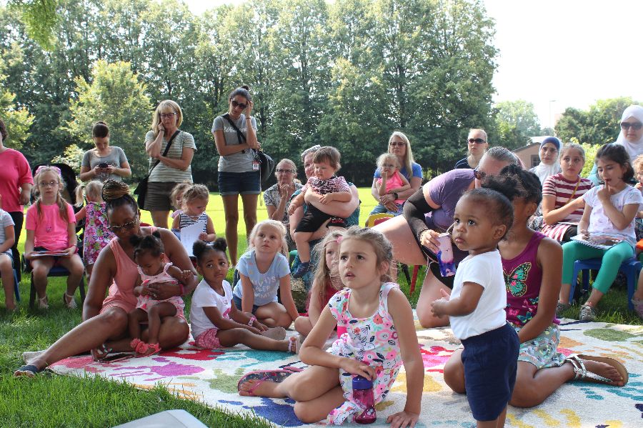 A group of children and families listen to storytime outside at Applewood