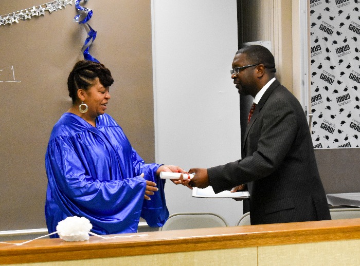 A woman in a commencement gown receives her certificate