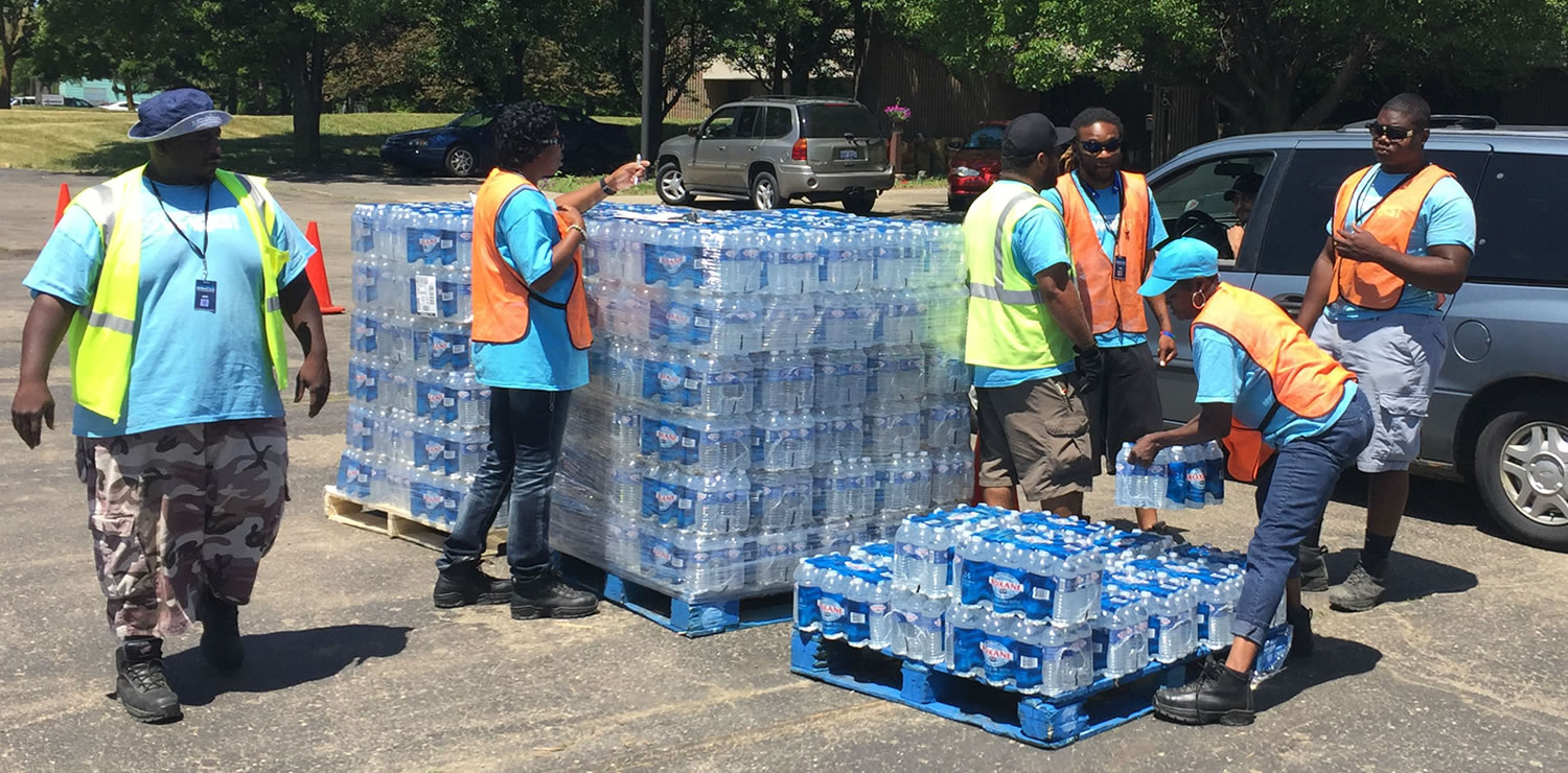 People in vests moving cases of water.