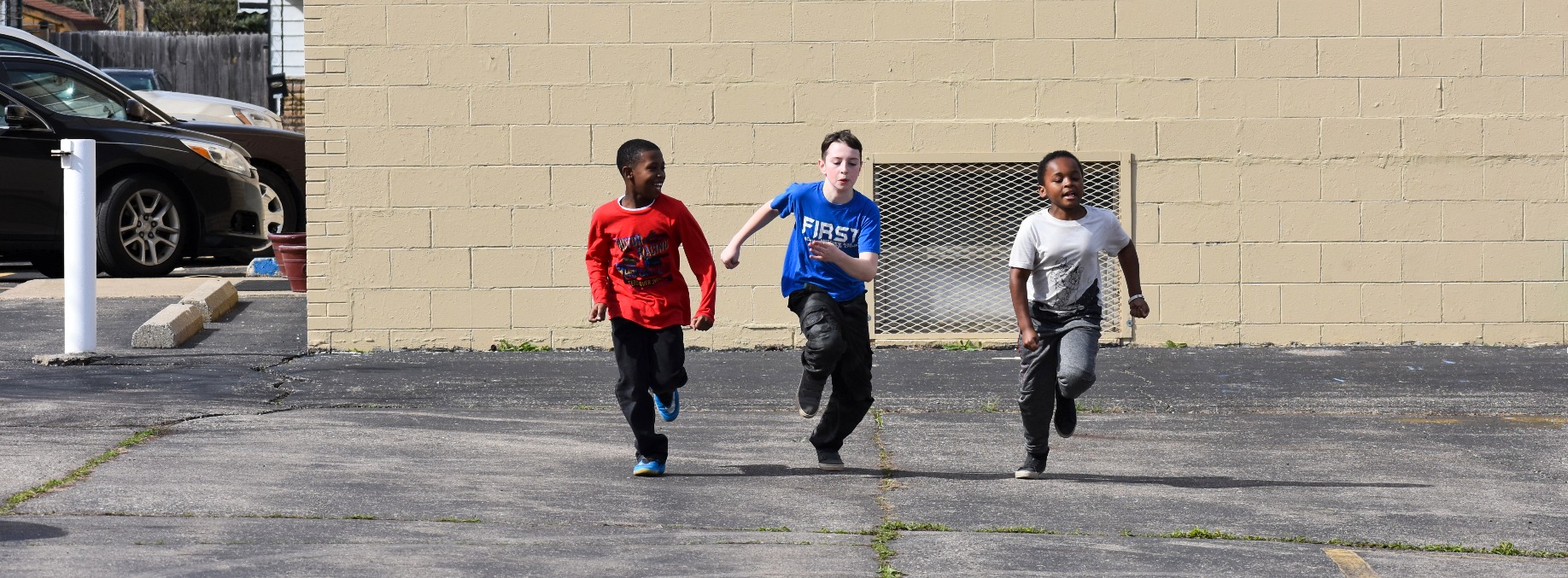 Three boys race each other across an empty lot