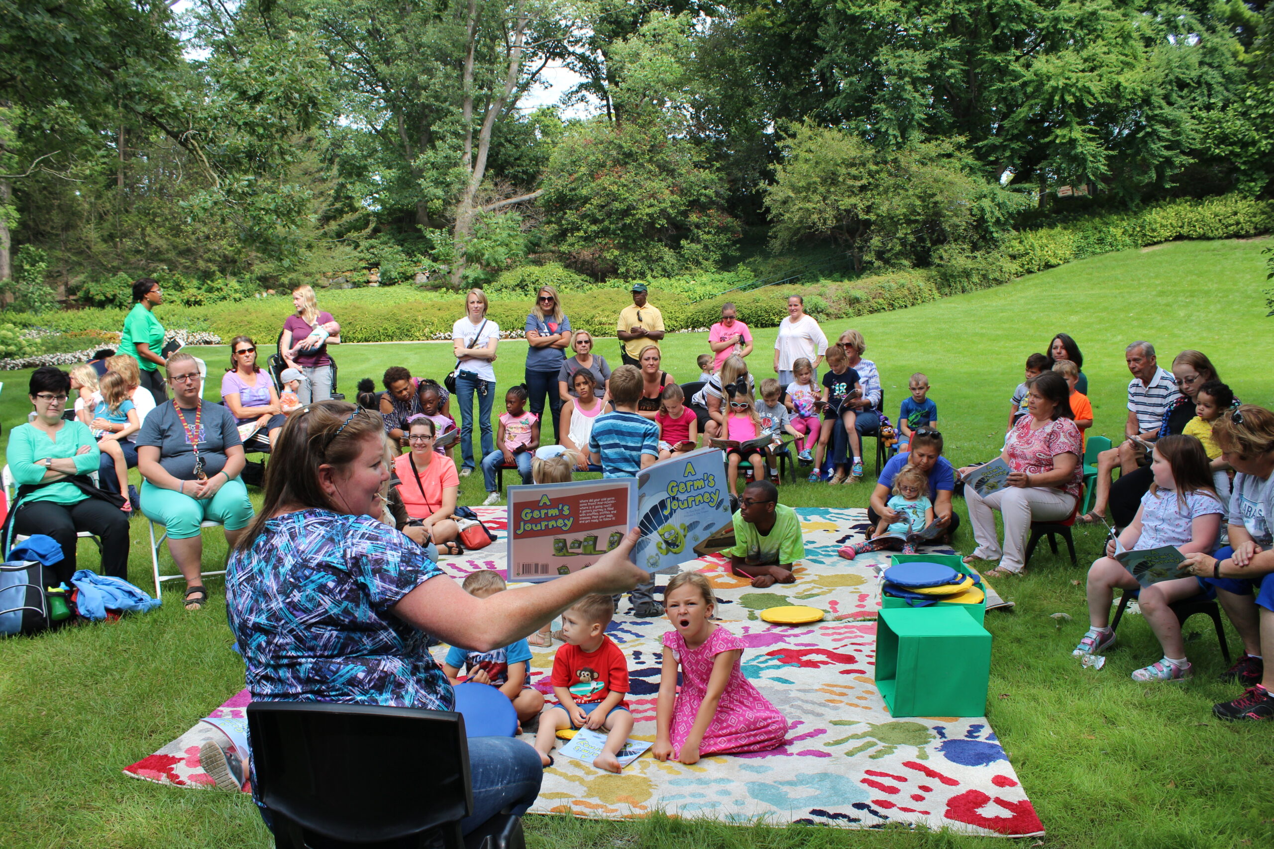 https://www.ruthmottfoundation.org/wp-content/uploads/2021/04/woman-reading-to-kids-outside-at-storytime-at-applewood-scaled.jpg