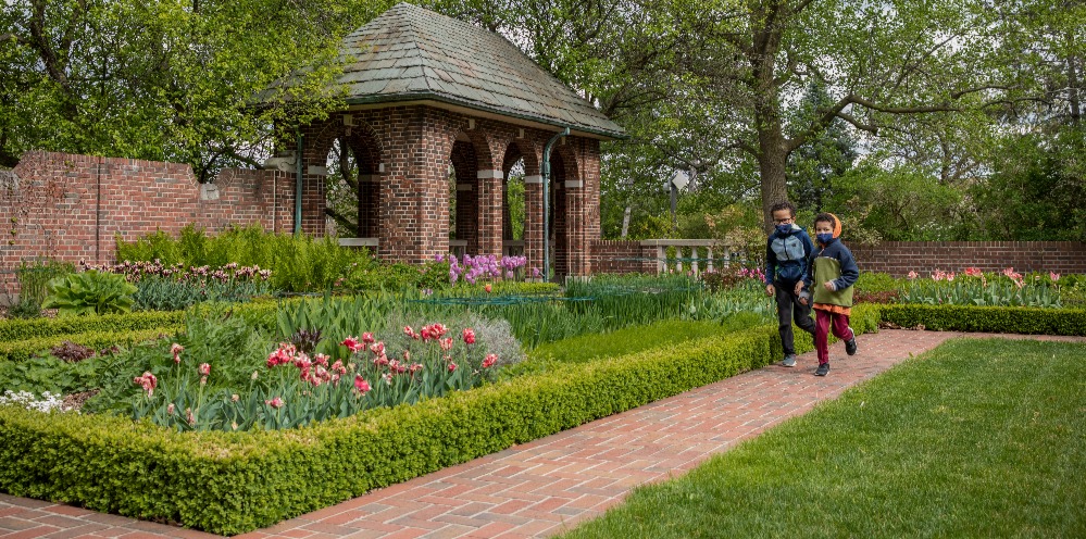 Two boys wearing face masks run through the perennial garden at Applewood