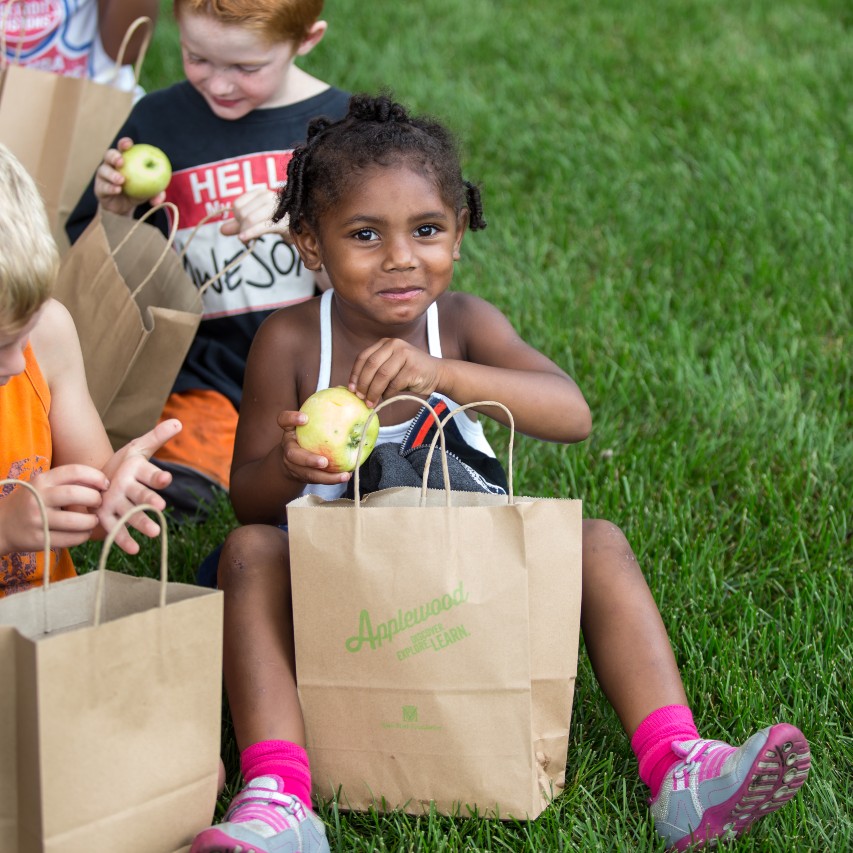 A young person sits on the grass eating an apple out of an 