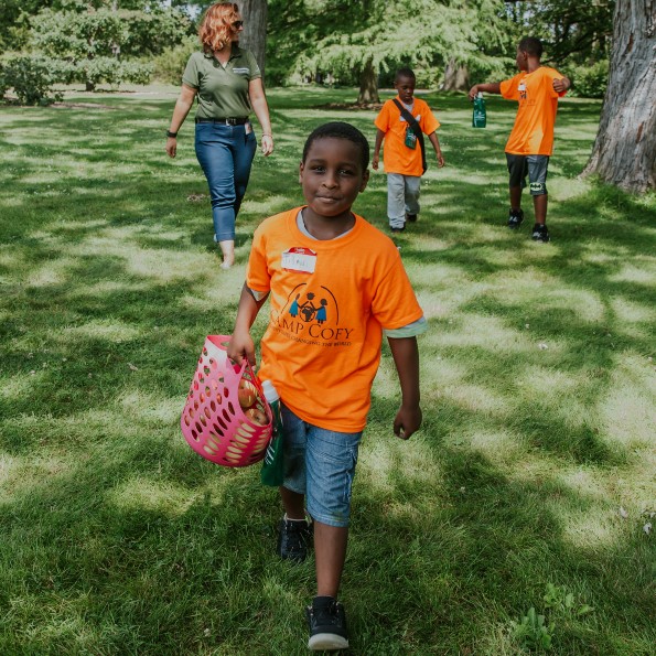 A youth in an orange tshirt carries a basket of apples at Applewood