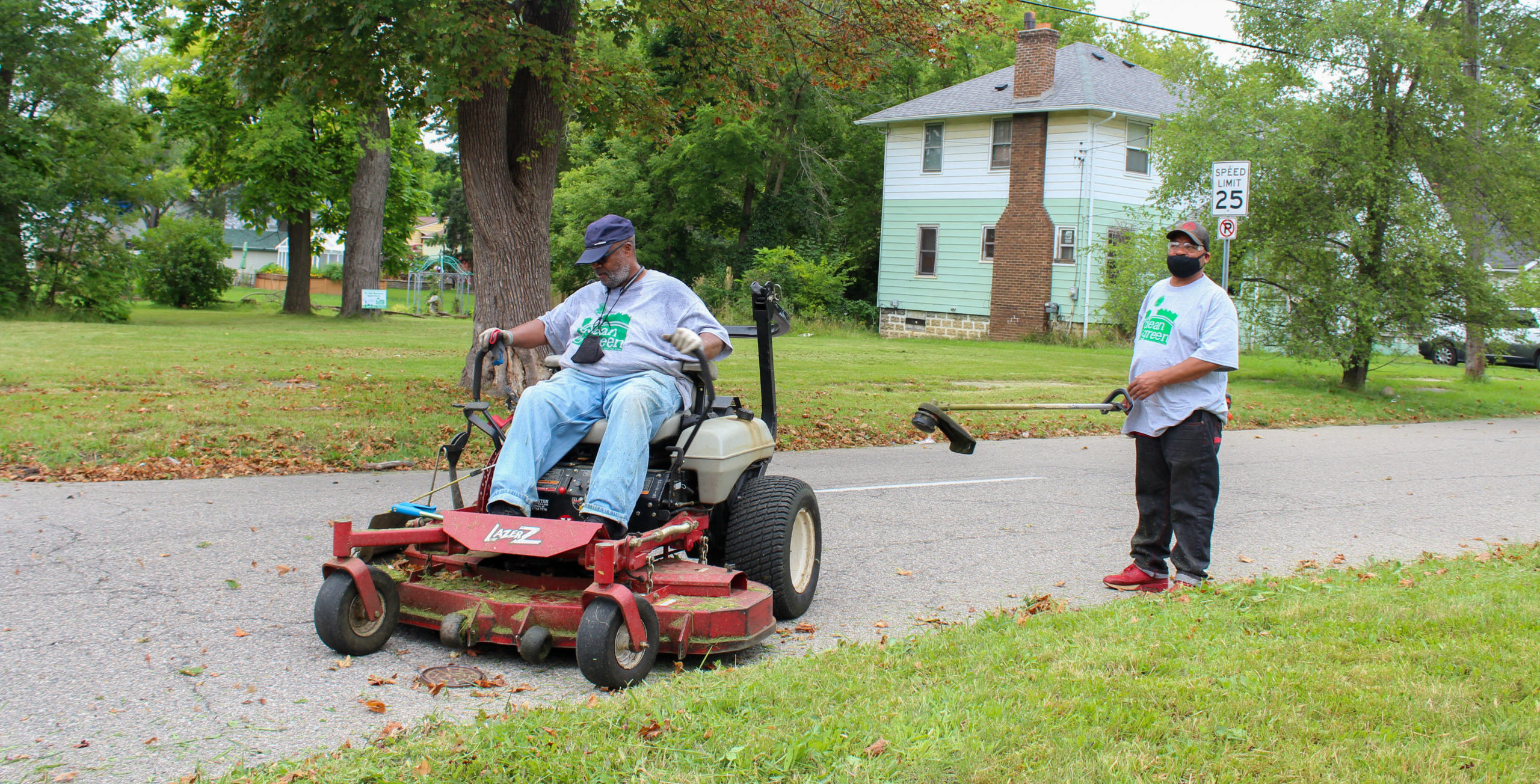 Two men wearing gray Clean & Green T-shirts operate lawn equipment