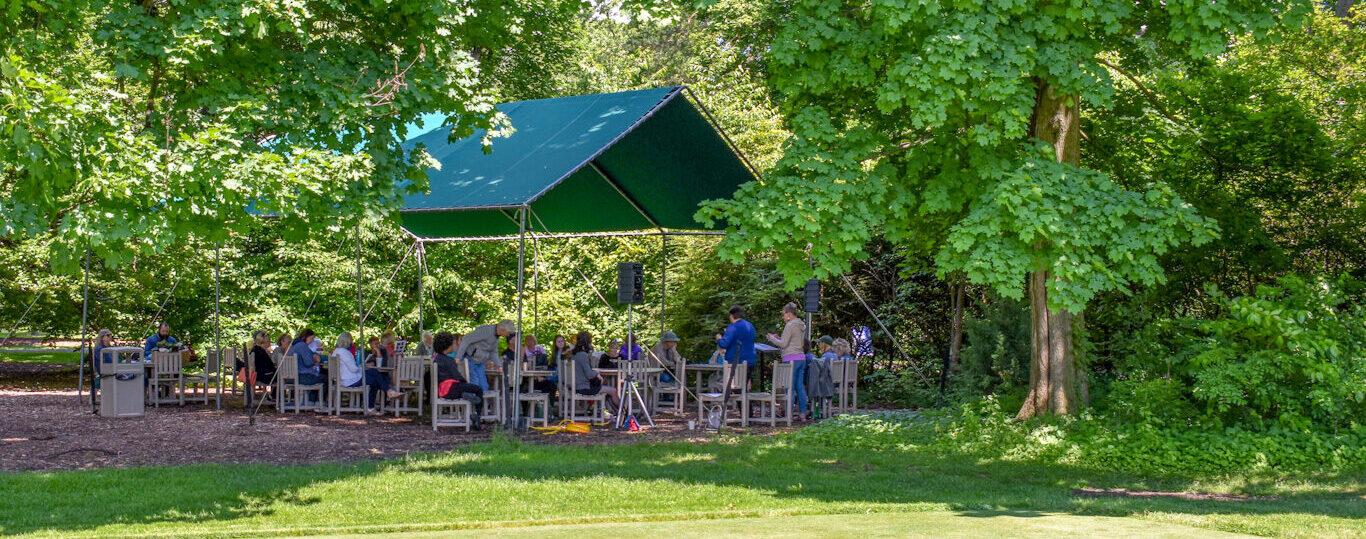 Attendees sit in Applewood's covered seating area listening to a woman's presentation