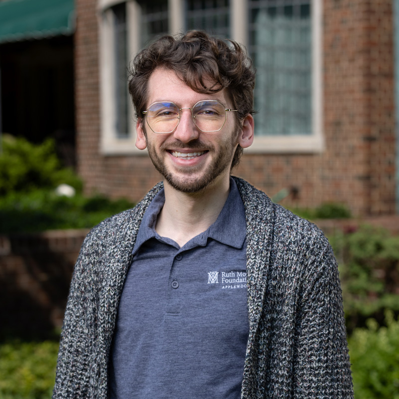 A man with glasses smiling in front of a building.