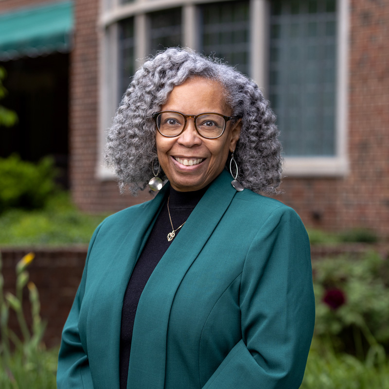 An african-american woman in a green jacket standing in front of a brick building.