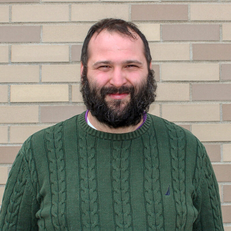 A man with a beard standing in front of a brick wall.