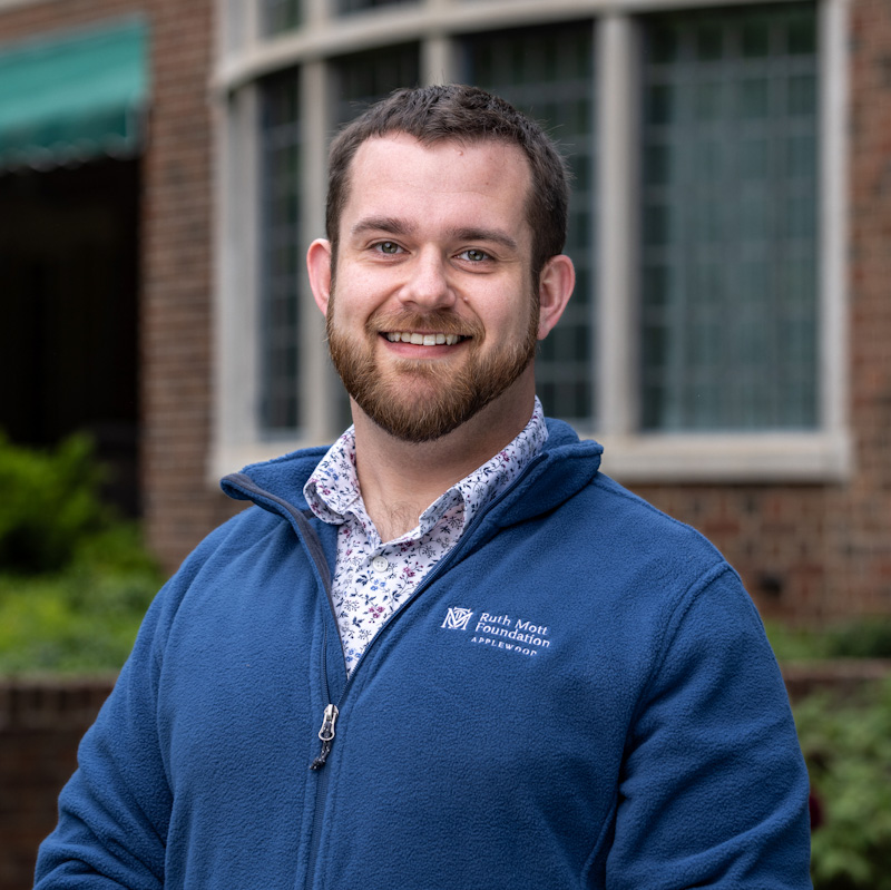 A man in a blue jacket smiling in front of a brick building.