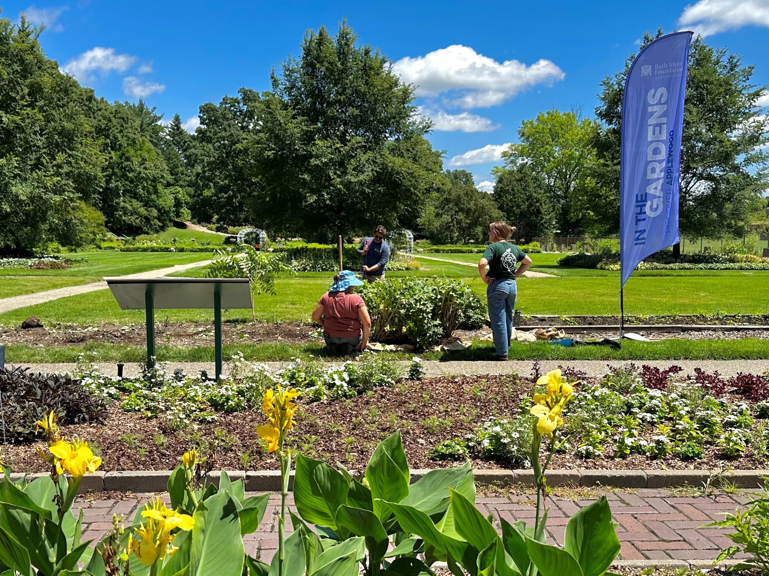 Three people work on a garden plot near a large blue feather banner that reads 