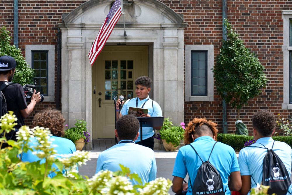 A boy in a collared blue shirt stands in front of a group of boys in blue shirts in front of the house at Applewood.