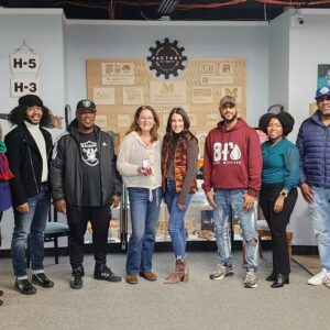 A group of eight adults posing for a photo in a room with industrial-themed decor and wall art.