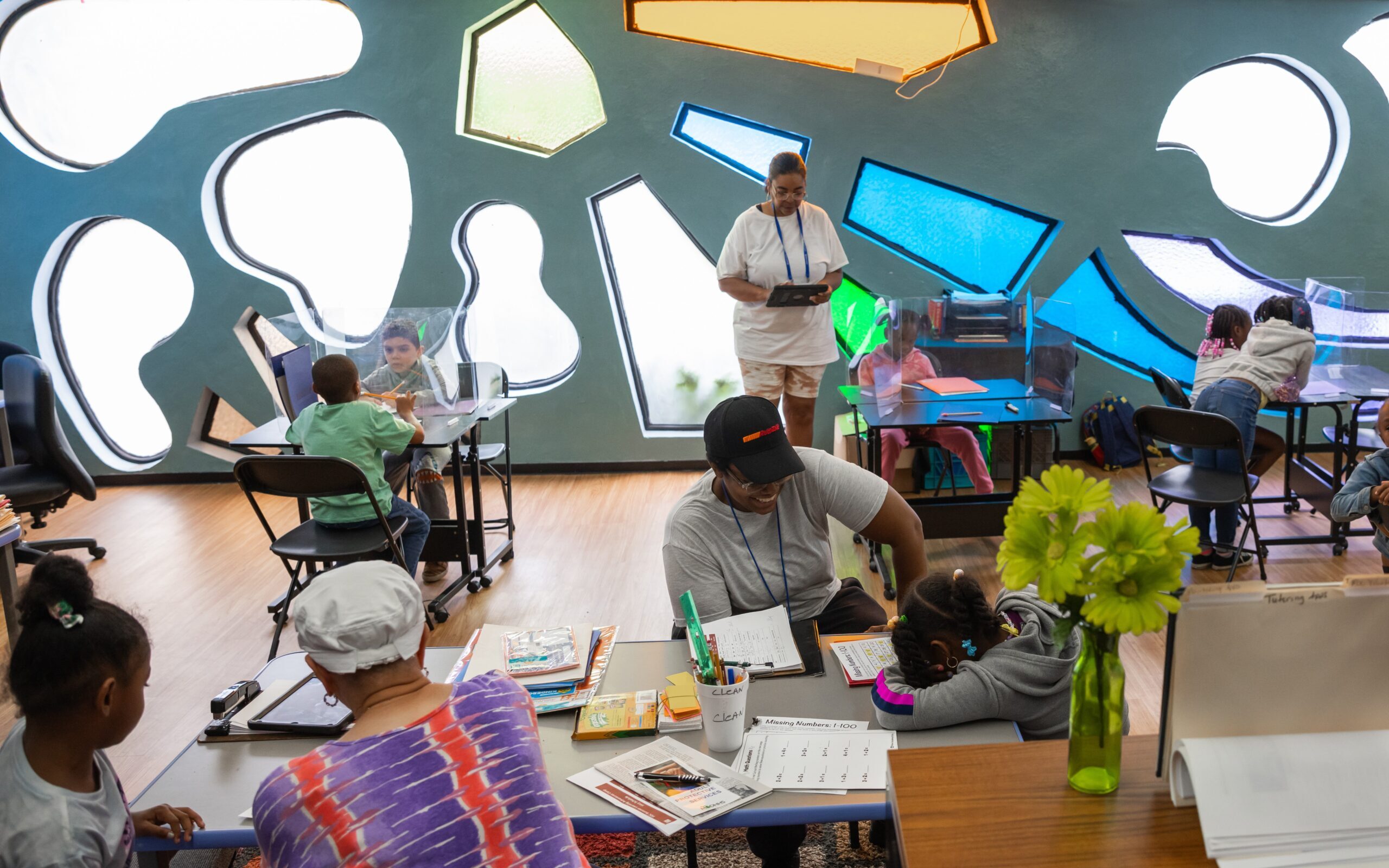 Children and adults engage in educational activities in a colorful classroom with unique wall cut-outs and modern furniture, sponsored by the Ruth Mott Foundation.