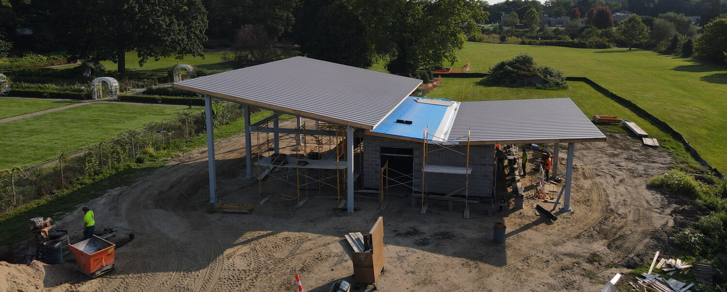A partially constructed building with a metal roof sits on a cleared plot of land, part of the Applewood Estate Master Plan. Construction materials and scaffolding are present around it, with trees and grass visible in the background.