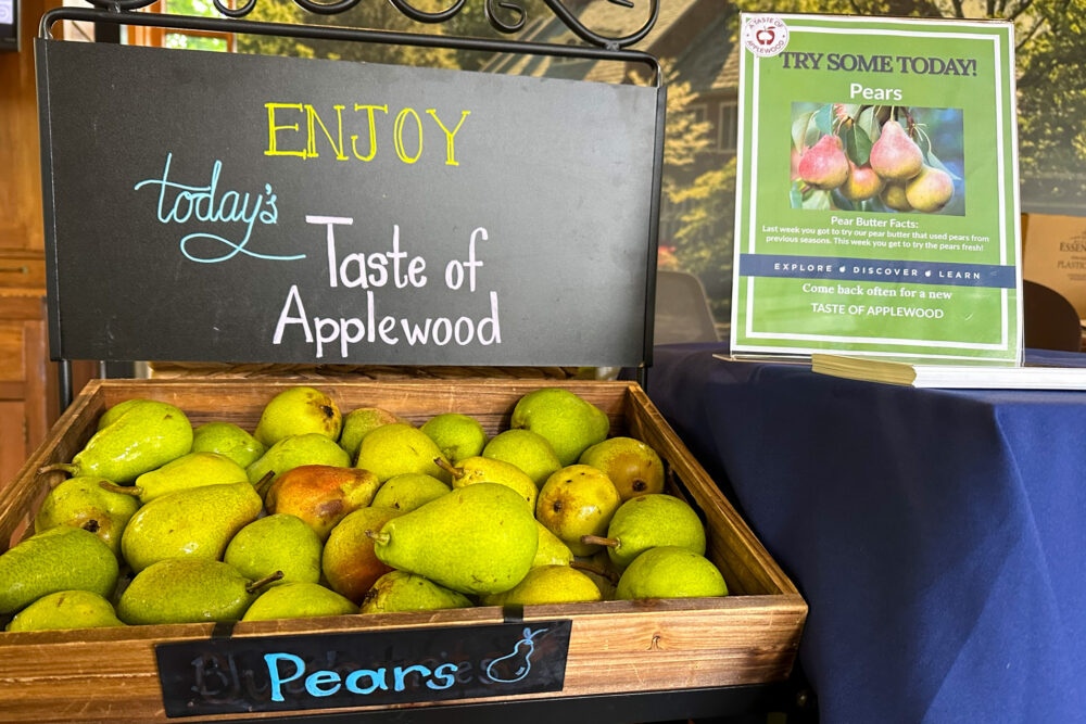 A wooden crate of pears is displayed below a sign reading 